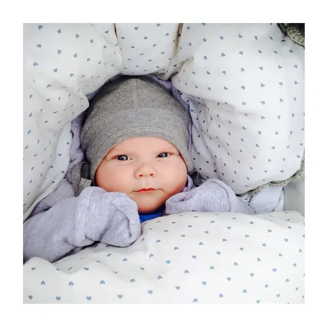 Baby med grå lue i vognen, omgitt av hvitt fôr med små lyseblå hjerter