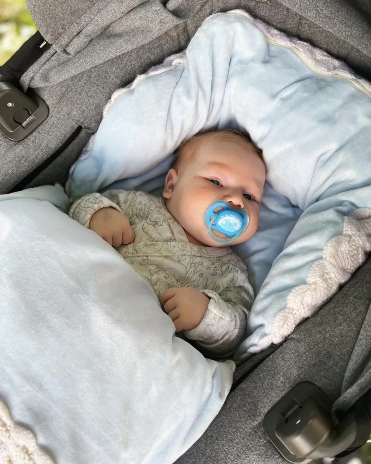 Baby med smokk ligger i vognen i en lyseblå pose