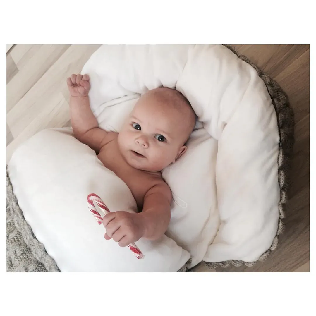 Baby ligger på en hvit pute med grå strikkekant og holder en polkagris