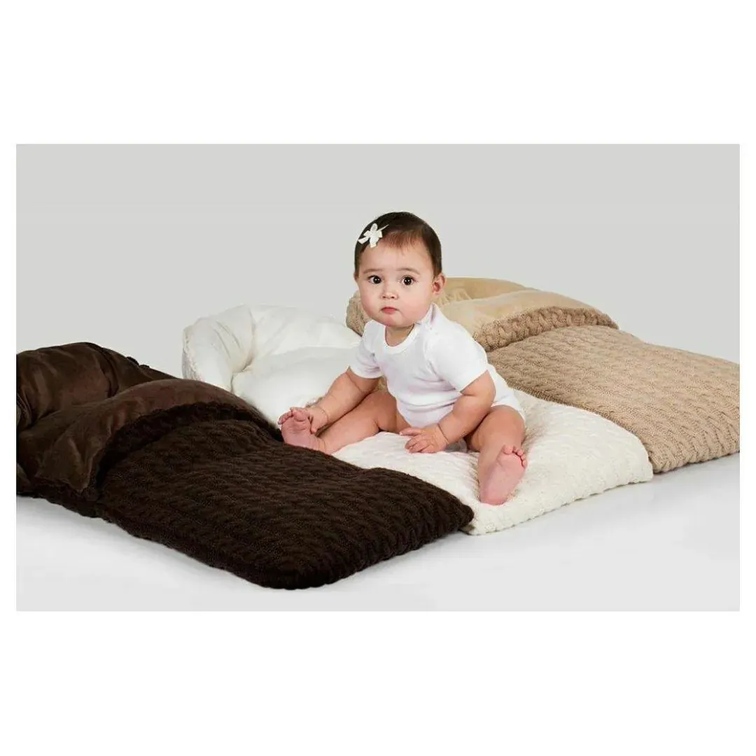 Baby sitter på vognposer i brun og beige kabelstrikk mot grå bakgrunn