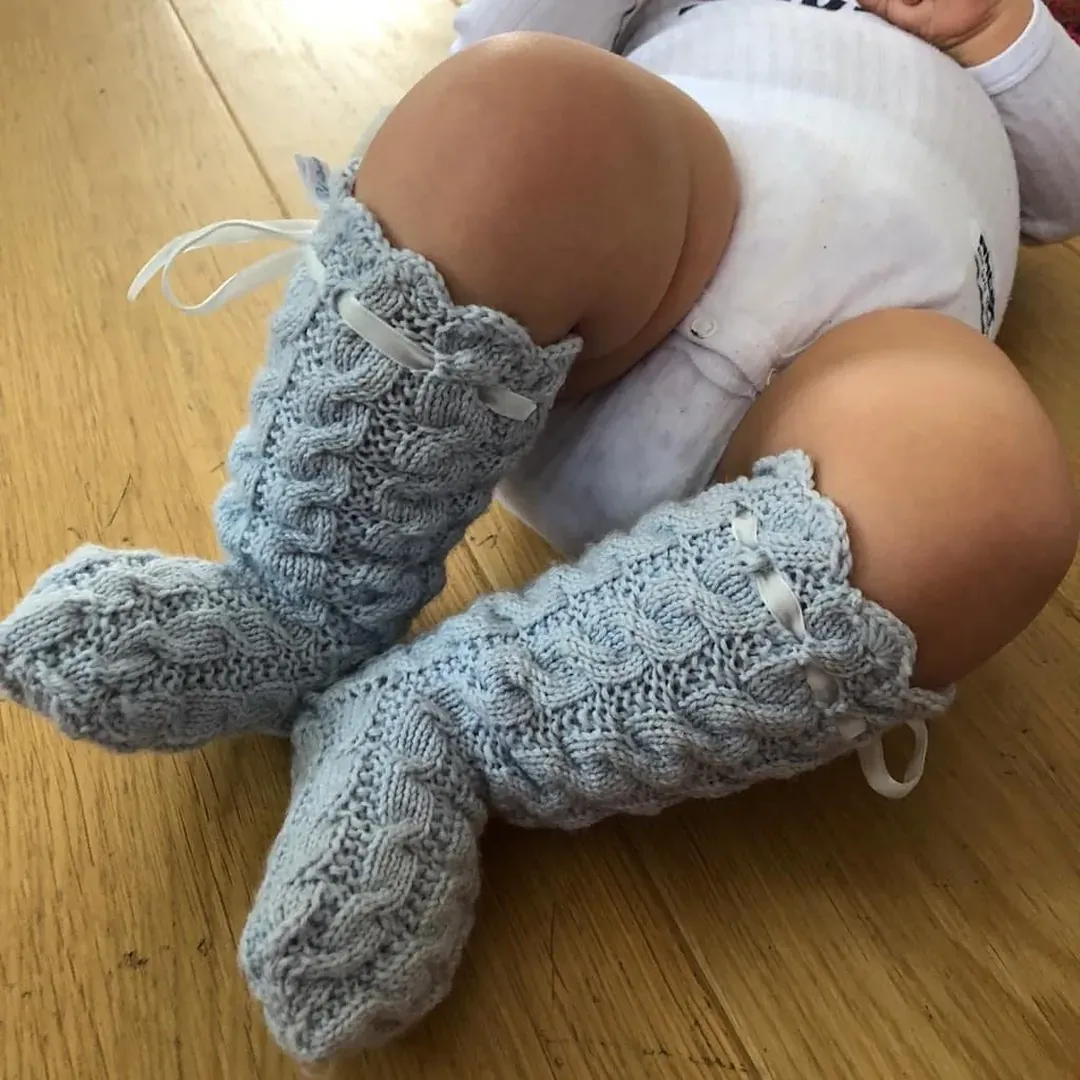 Baby med lyseblå strikkesokker i kabelstrikk på tregulv