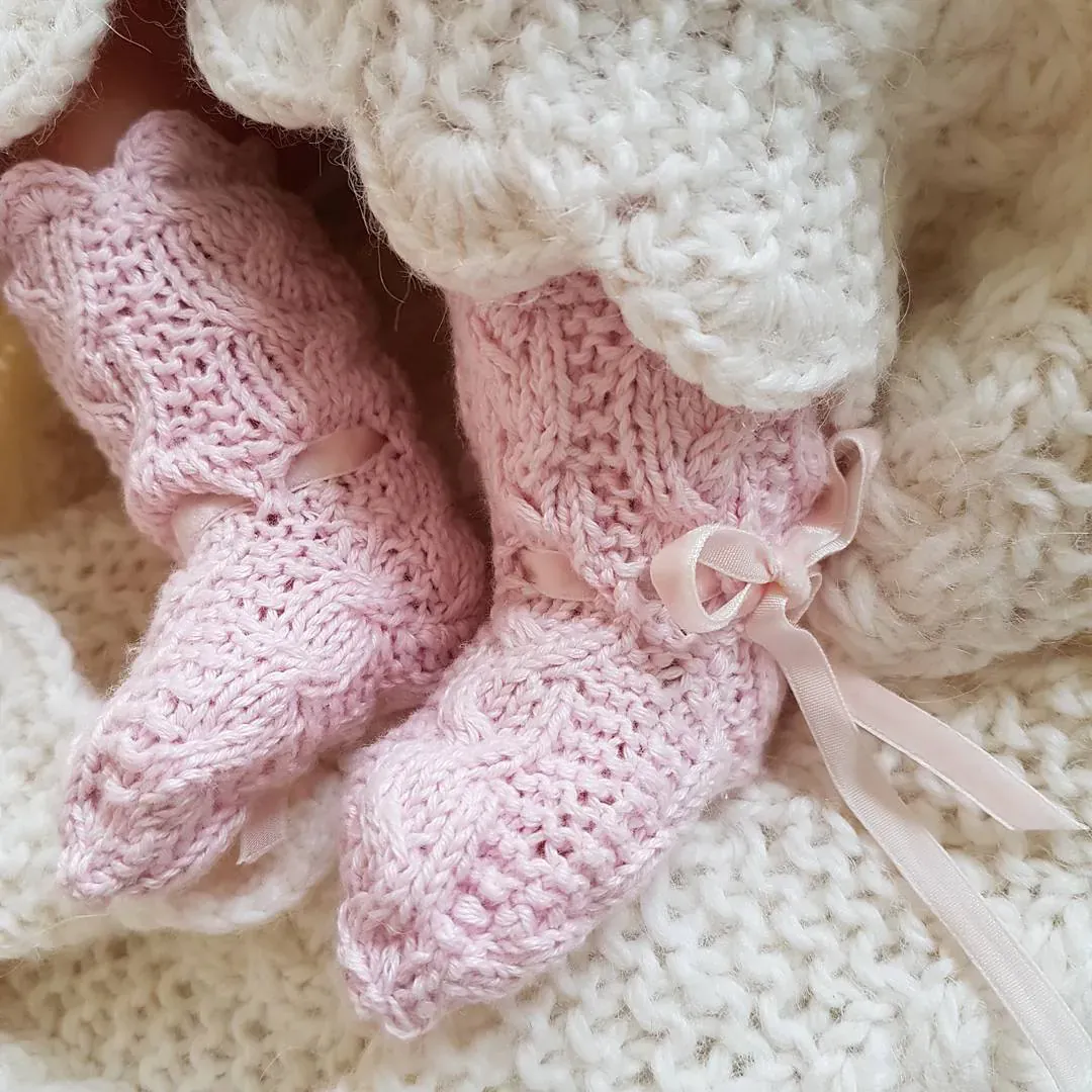 Rosa strikkede babysokker med silkebånd på kremhvit strikk