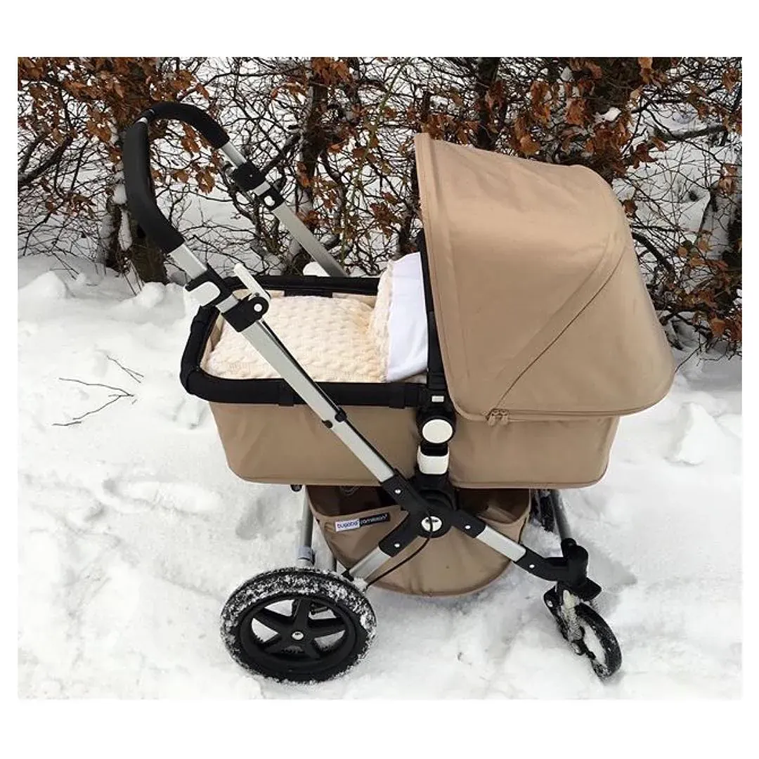 Beige barnevogn med vognpose i beige kabelstrikk ute i snøen