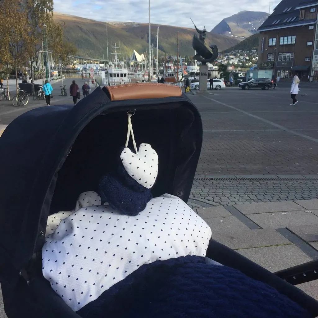 Barnevogn med vognpose i marine kabelstrikk og hvitt fôr med prikker, og et vognhjerte, i en by