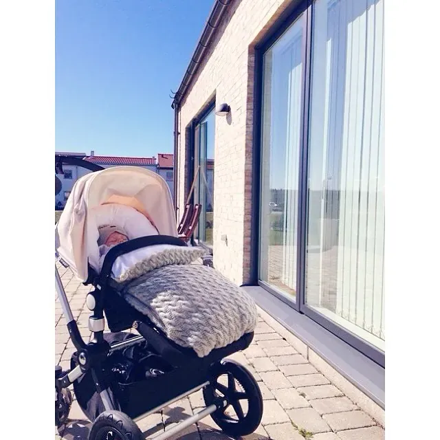 Barnevogn ute ved et hus med en baby i en vognpose i grå kabelstrikk