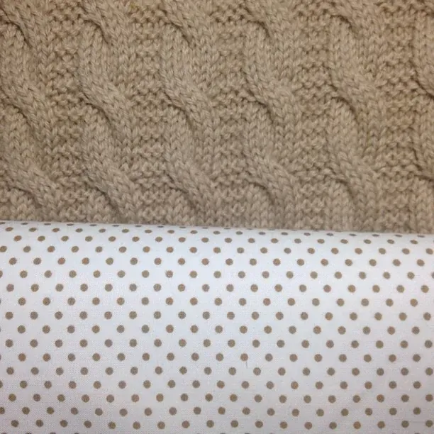 Nærbilde av beige kabelstrikk mot hvitt fôr med beige prikker