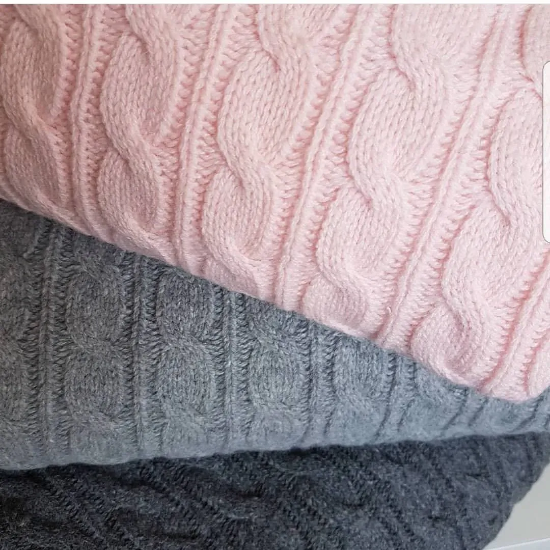 Nærbilde av kabelstrikk i rosa, grå og mørkegrå lagt i en stabel