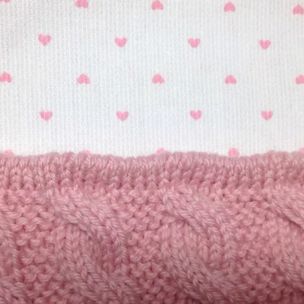 Nærbilde av rosa kabelstrikk mot hvitt fôr med små rosa hjerter