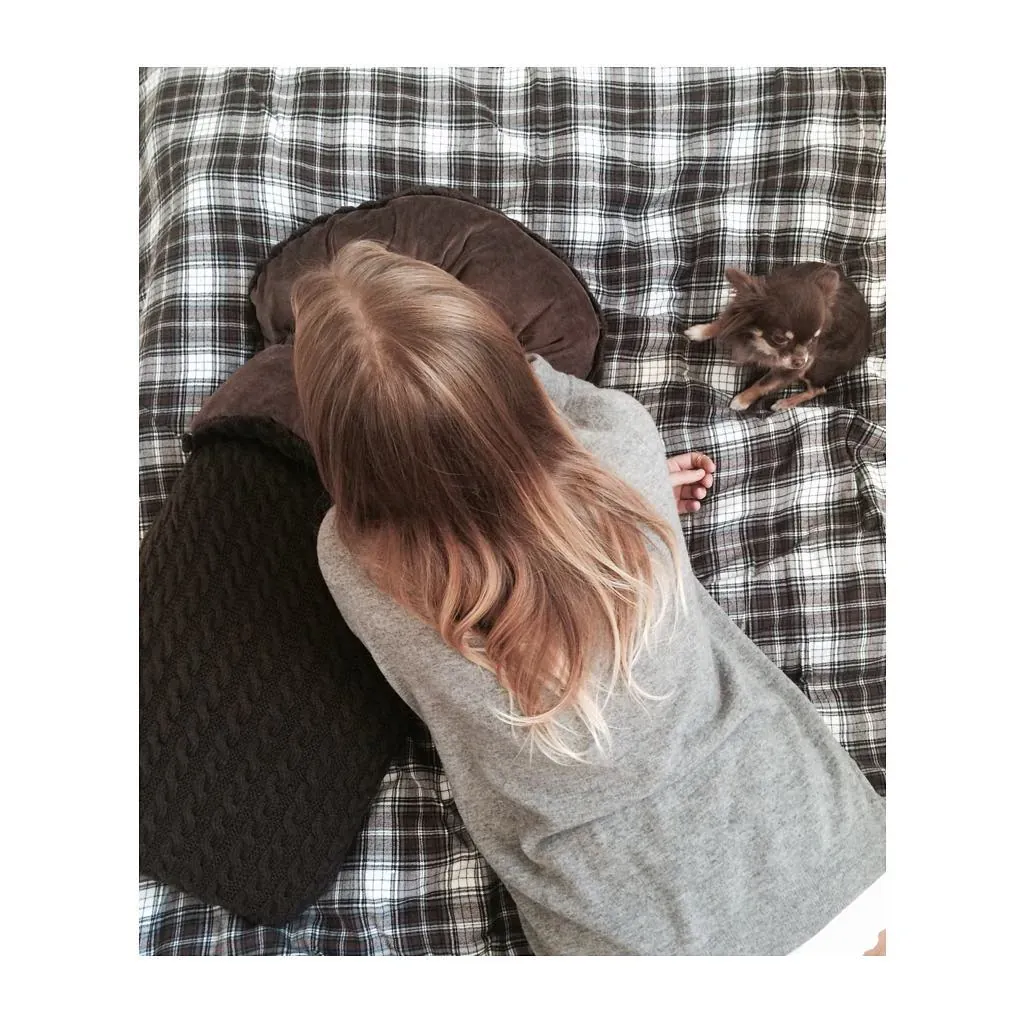 Lite barn ligger på et rutete pledd ved siden av en vognpose i brun kabelstrikk og en liten hund