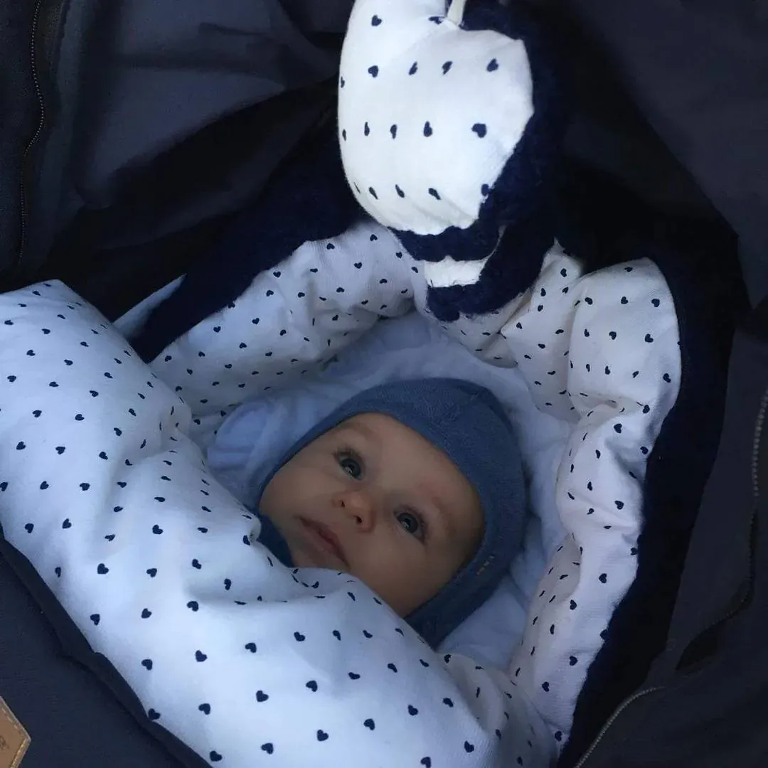 Baby med blå lue i vognen i en hvit pose med små marine hjerter