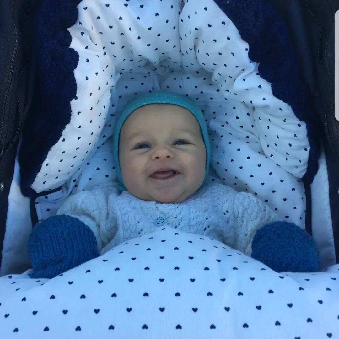 Baby smiler i vognen i en hvit pose med små marine hjerter