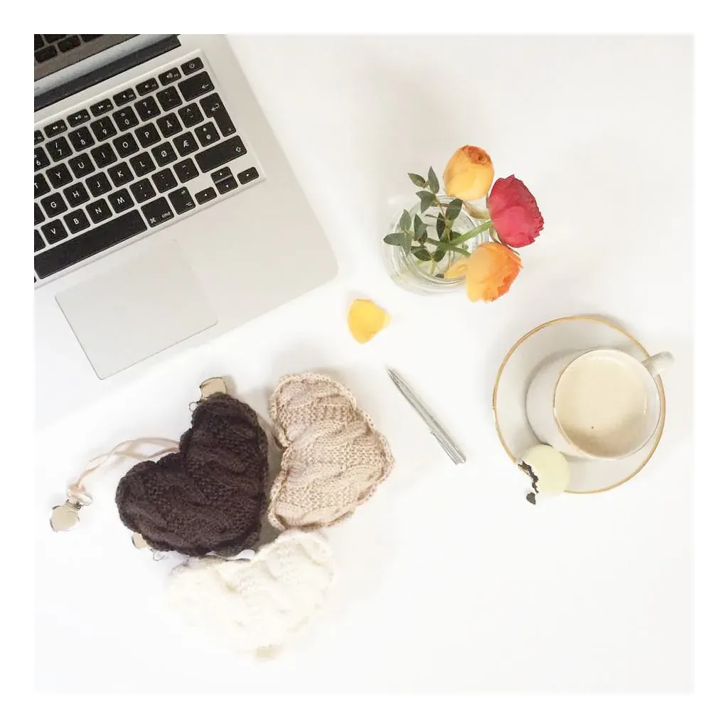 Vognhjerter i brun, beige og hvit strikk på et hvitt bord med laptop, kaffe og blomster