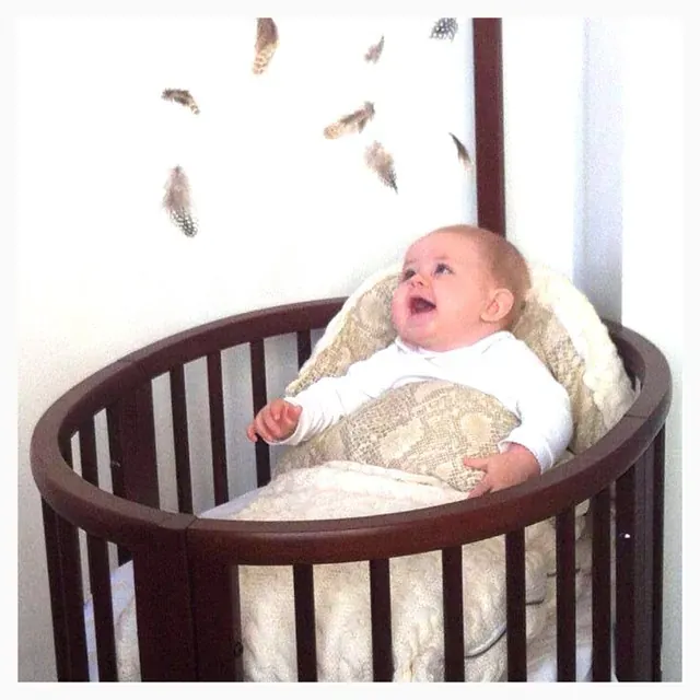 Smilende baby i en beige vognpose i en rund sprinkelseng