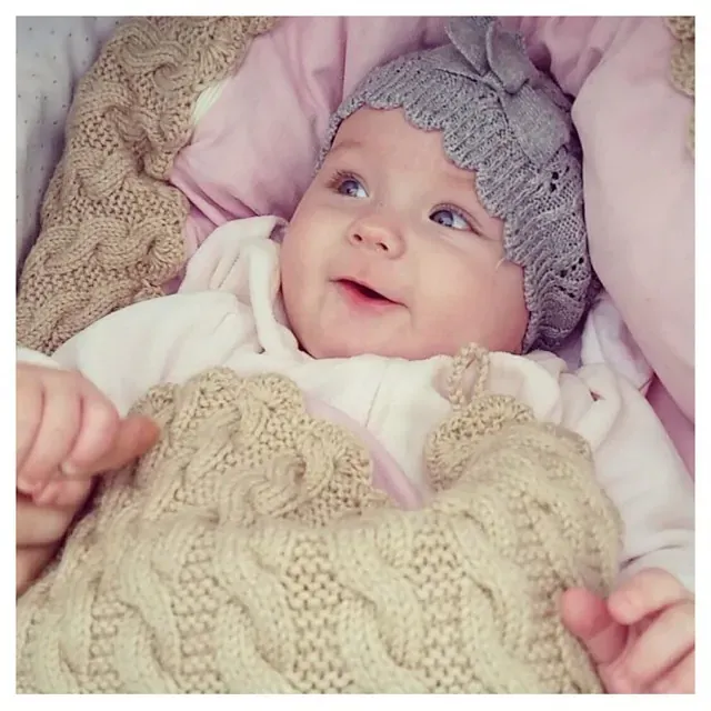 Baby med grå strikkelue i en vognpose i beige kabelstrikk