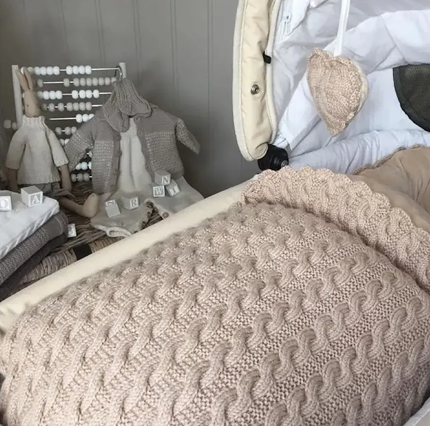 Vognpose i beige kabelstrikk i vognen, med et beige vognhjerte hengende i kalesjen