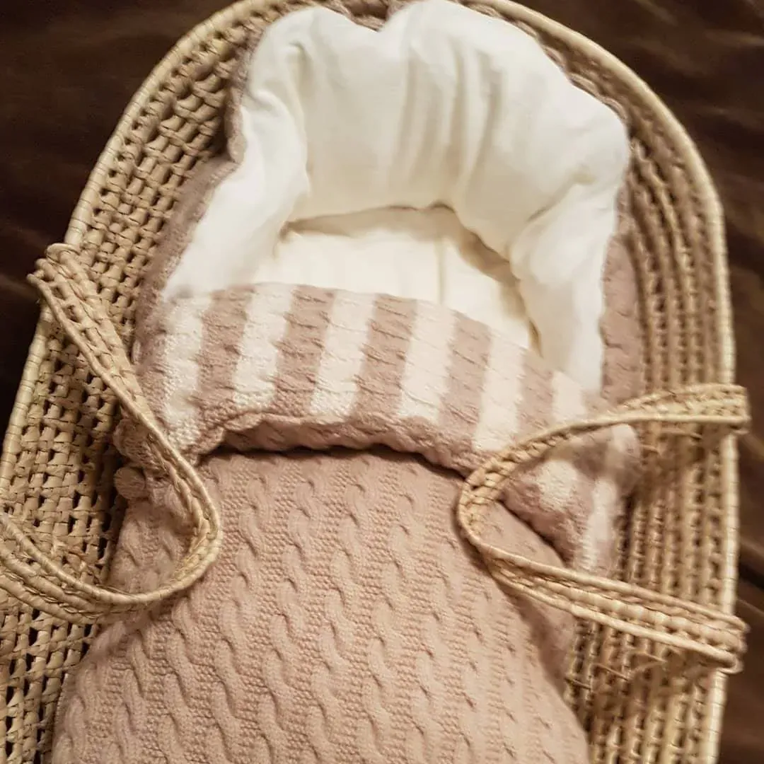 Vognpose i beige kabelstrikk med stripet kant og hvitt fôr i en flettet kurv