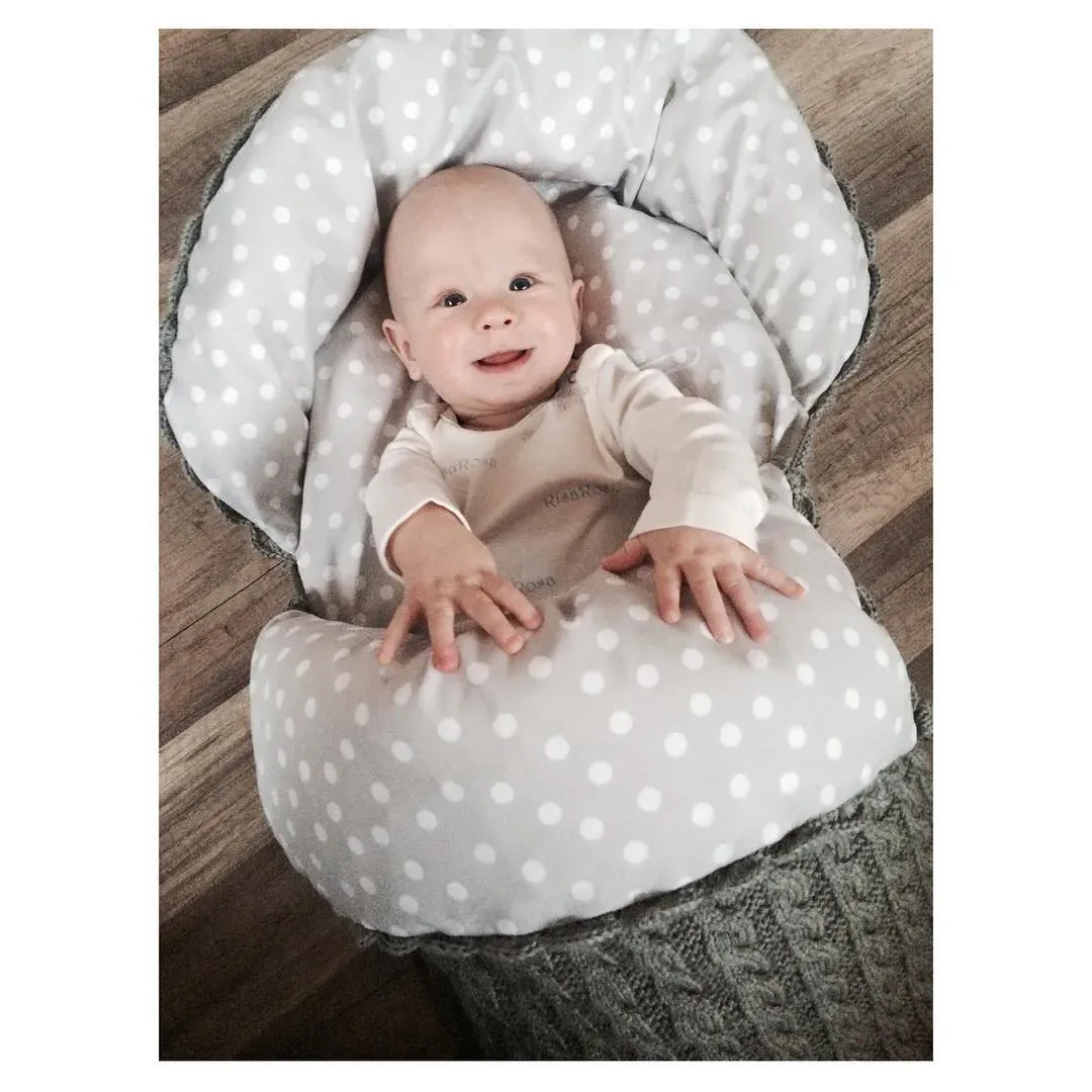 Baby smiler i vognpose i grå kabelstrikk med grått prikkete fôr