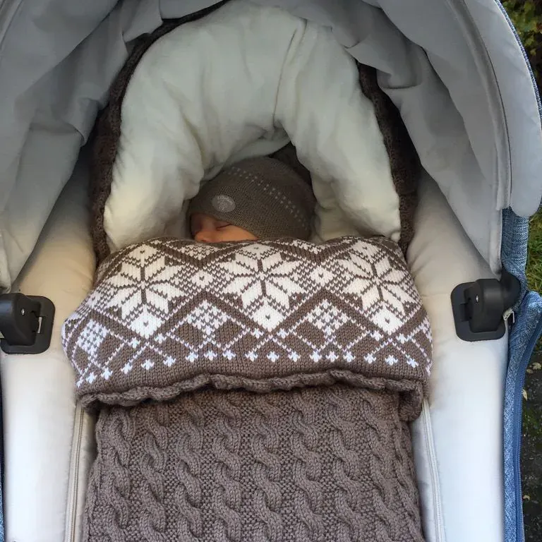 Baby sover i vognen i en vognpose i grå kabelstrikk med stjernemønster