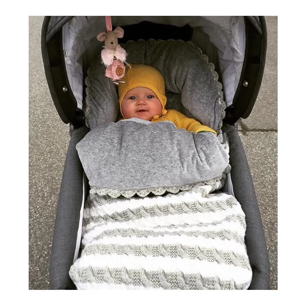 Baby i gul lue i vognen, i vognpose i hvit og grå stripet kabelstrikk med grått fôr