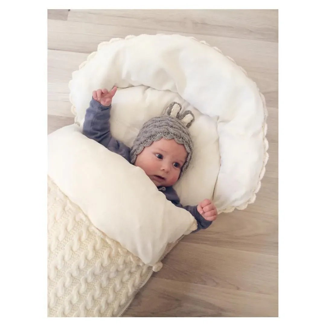 Baby med kaninlue i vognpose i kremhvit kabelstrikk med kremhvitt fôr