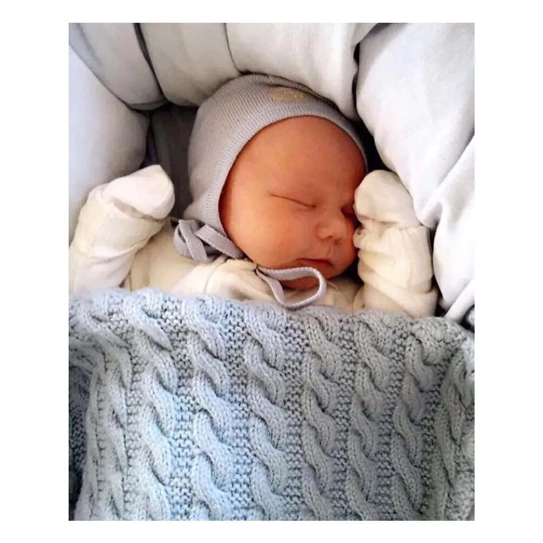 Nyfødt baby sover i vognen under vognpose i lyseblå kabelstrikk