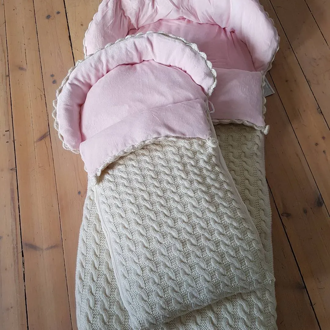 Vognpose i lysegrå kabelstrikk med rosa fôr på tregulv