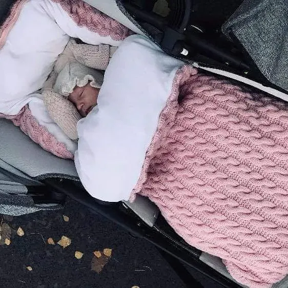 Baby sover i vognen i vognpose i rosa kabelstrikk med hvitt fôr