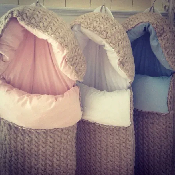 Tre hengende vognposer i beige kabelstrikk med rosa, kremhvitt og lyseblått fôr