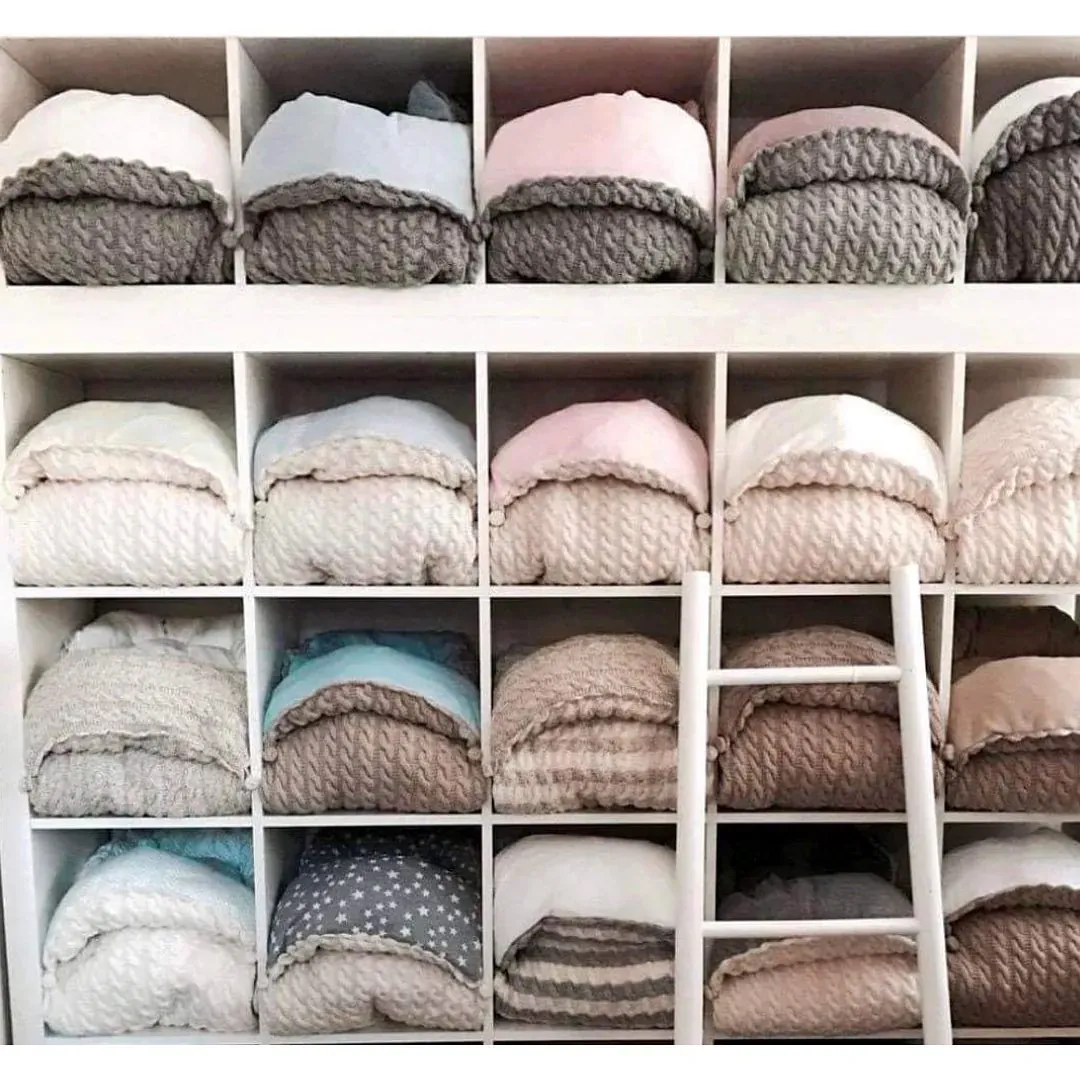 Hyller fylt med vognposer i kabelstrikk i grått, rosa, beige, hvitt og brunt