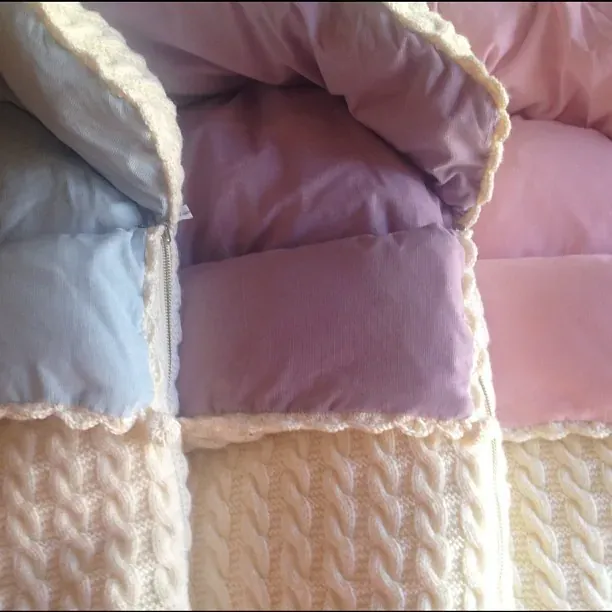 Tre vognposer i kremhvit kabelstrikk med lyseblått, lilla og rosa fôr side om side