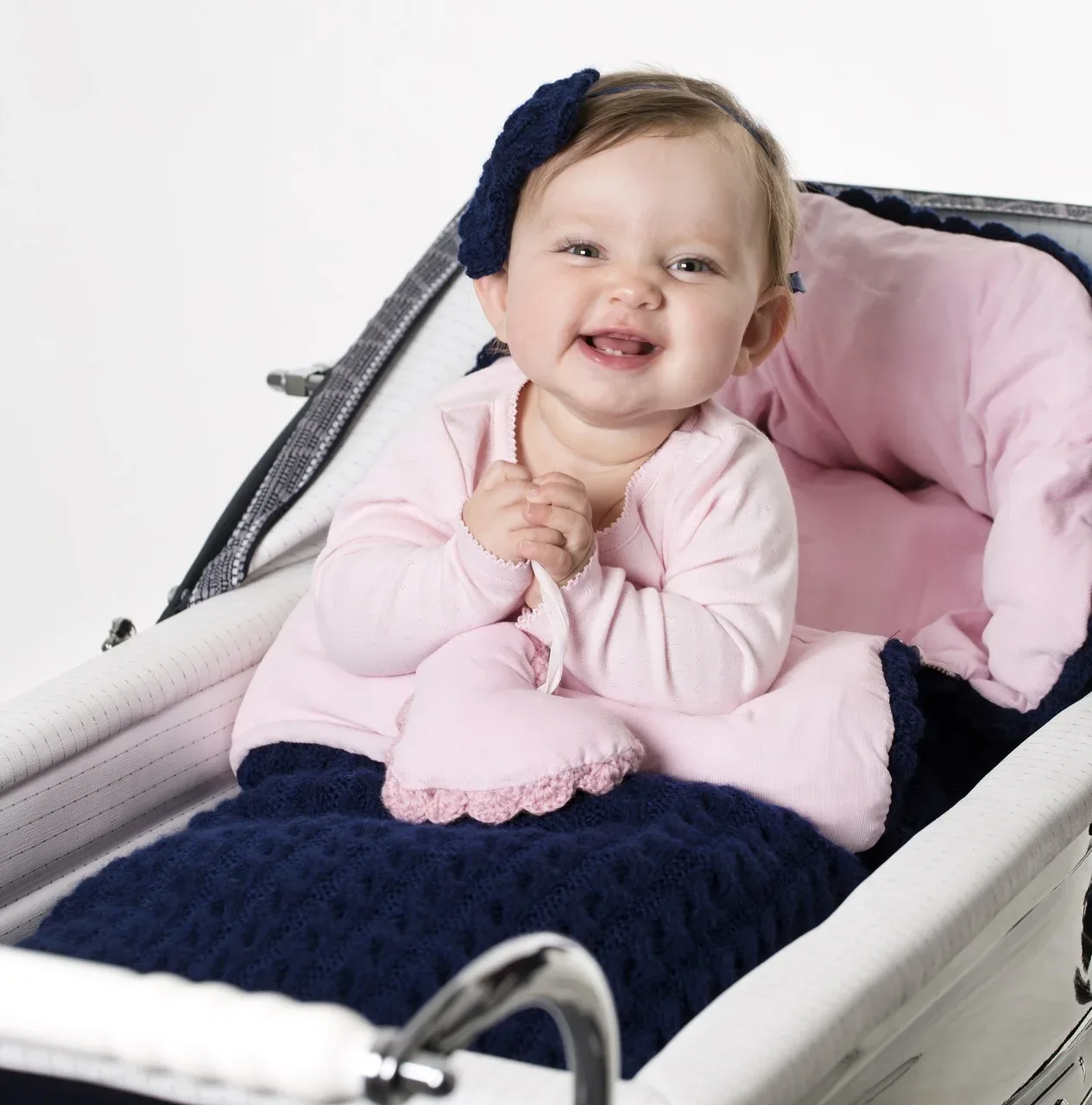 Smilende baby i vogn med marineblå vognpose og rosa fôr