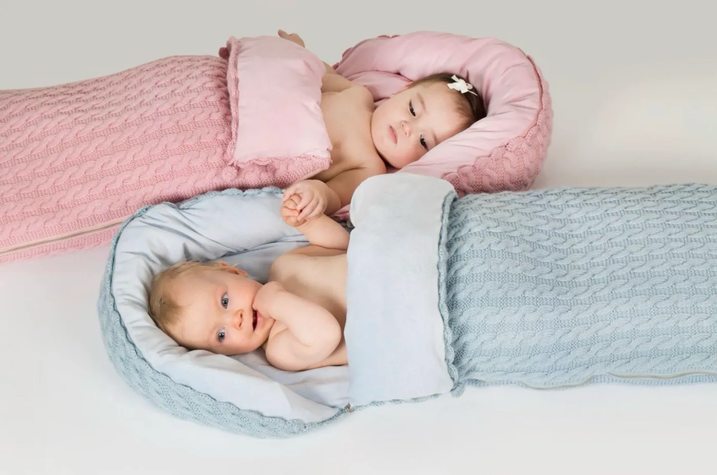 To babyer i vognposer i kabelstrikk, en med rosa og en med lyseblått fôr